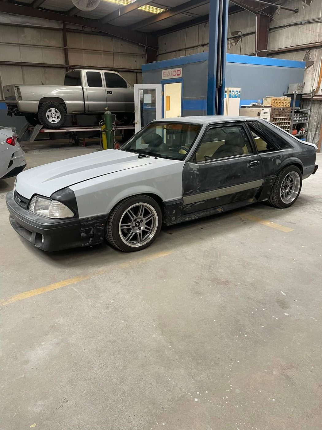Fox-body Mustang in primer and bodywork inside the Straightline shop